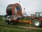 Трактор выставляет барабаную дождевальную установку на позицию для полива